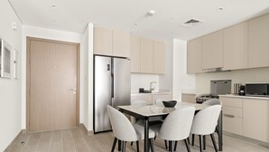 A modern kitchen with a dining area, featuring a refrigerator, stove, microwave, and a dining table with chairs. - Lotus at Creek Beach 1 - 407 2BD (Dubai)
