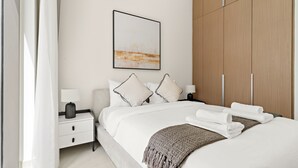 A modern hotel room with a large bed, a nightstand, a bedside table, a wardrobe, and a framed artwork on the wall. - Lotus at Creek Beach 1 - 407 2BD (Dubai)