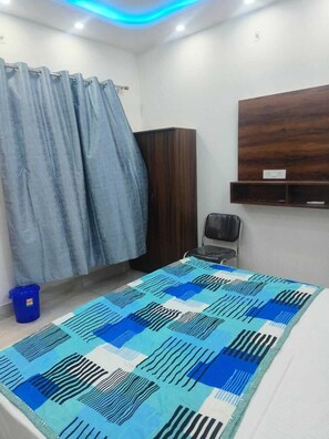 A bedroom with a bed, a wardrobe, a chair, and a blue bucket. - Hotel Sita Palace  (Faizabad)