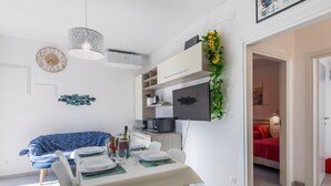 A modern living space with a dining area, a sofa, a TV mounted on the wall, and a kitchen area. - Casa Emma by Interhome (Cecina)