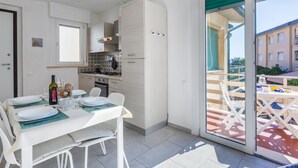 A modern kitchen with white cabinets, a dining table set for four, and a sliding glass door leading to an outdoor patio. - Casa Emma by Interhome (Cecina)
