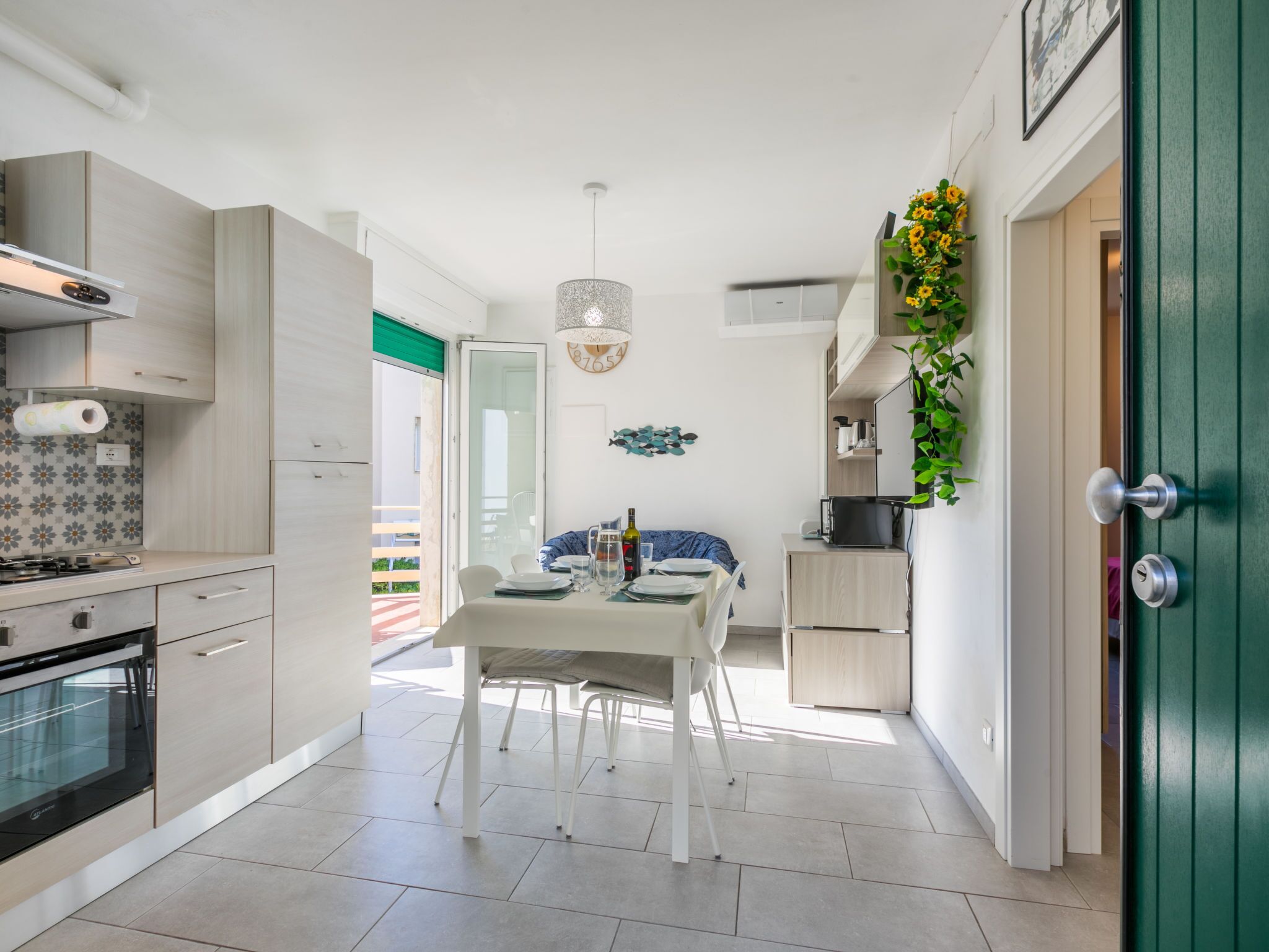 A modern kitchen with a dining area, a green door, and a view of the outdoors.