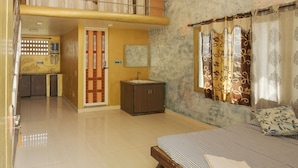 A spacious living area with a high ceiling, a balcony, a bed, a small cabinet, and a window with curtains. - Sunshine Guest House (Tiruvannamalai)