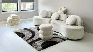 Un salon moderne avec un canapé blanc, un pouf rond et un tapis noir et blanc.
