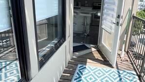 Un bâtiment moderne avec une façade dotée de grandes fenêtres, une cuisine ouverte et un tapis bleu à motifs sur la terrasse.