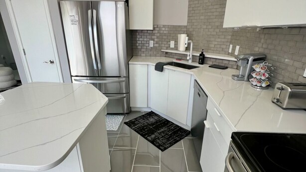 Une cuisine moderne avec des meubles blancs, un réfrigérateur en acier inoxydable, une machine à café et une cuisinière noire.