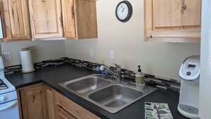 A kitchen with wooden cabinets, a stainless steel sink, a clock, and a coffee maker.
