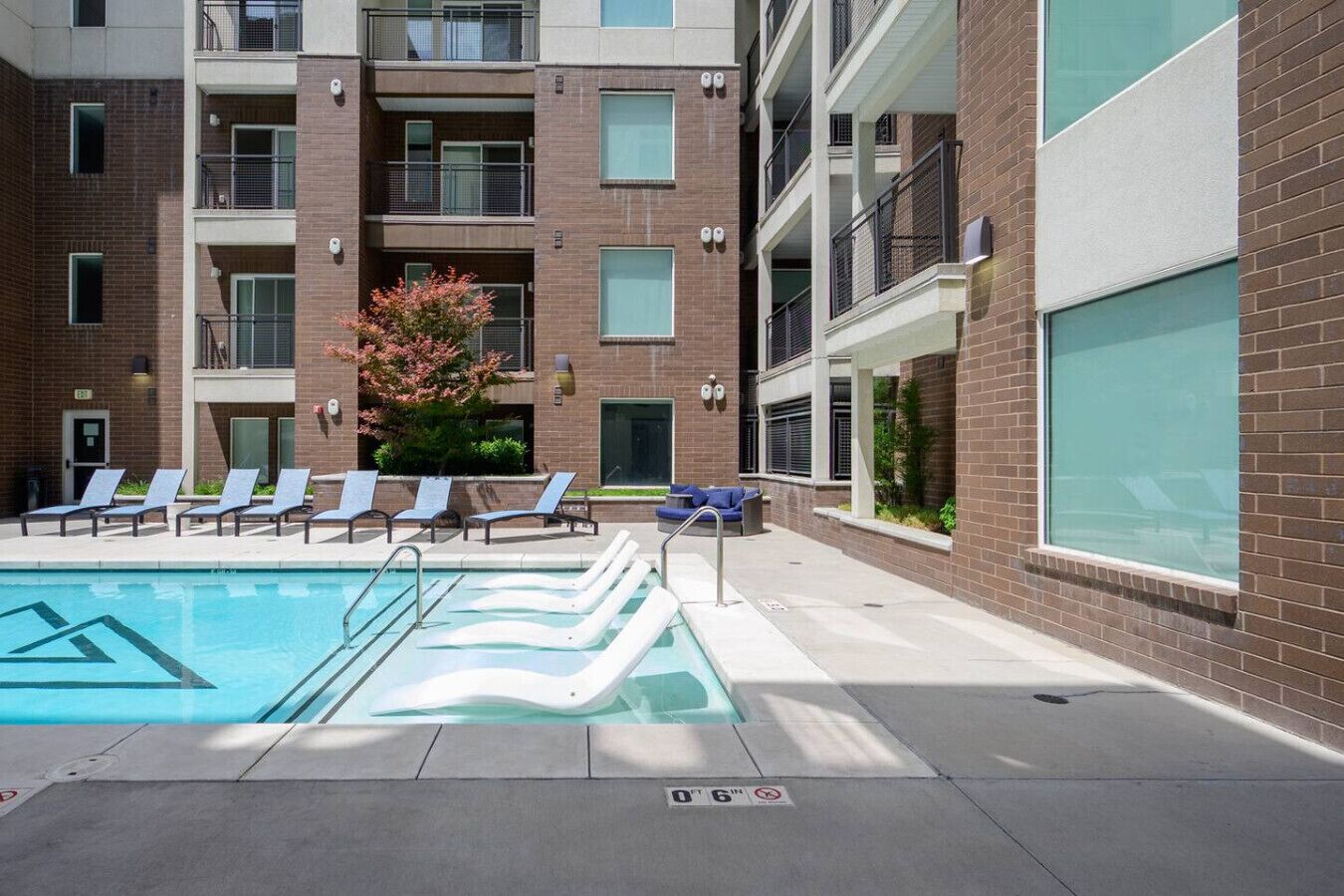 A pool area with lounge chairs and a small seating area, surrounded by a multi-story building with balconies.