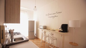 A modern kitchen with a refrigerator, microwave, and coffee machine. There are two white bar stools and a hanging light fixture. - Relax in an apartment in the city center (Palermo)