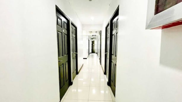 A long, narrow hallway with white walls and black-framed doors, leading to a room at the end. - Cosmo Hotel (Quezon City)