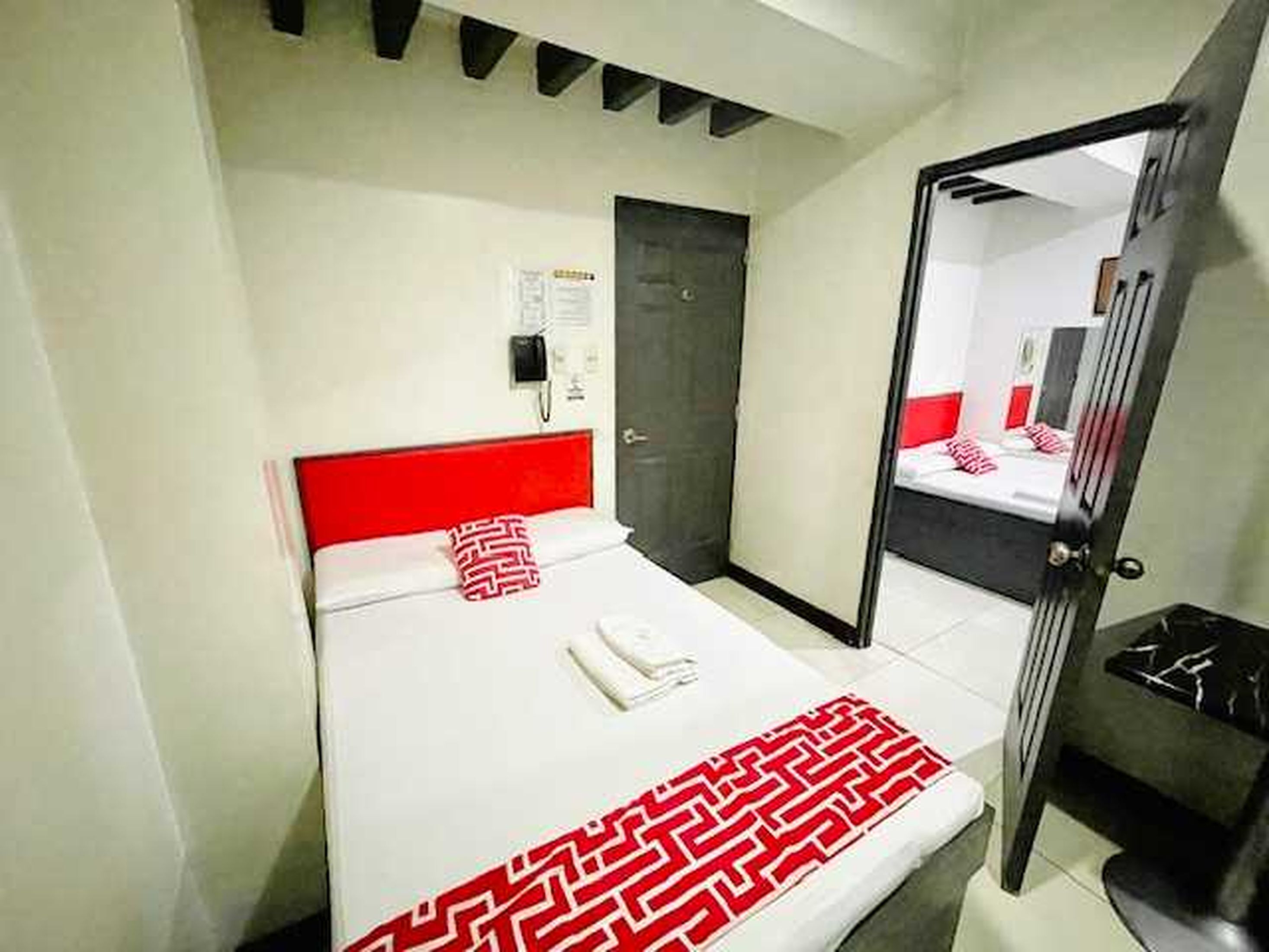 A hotel room with a bed, a mirror, a door, and a wall-mounted phone.