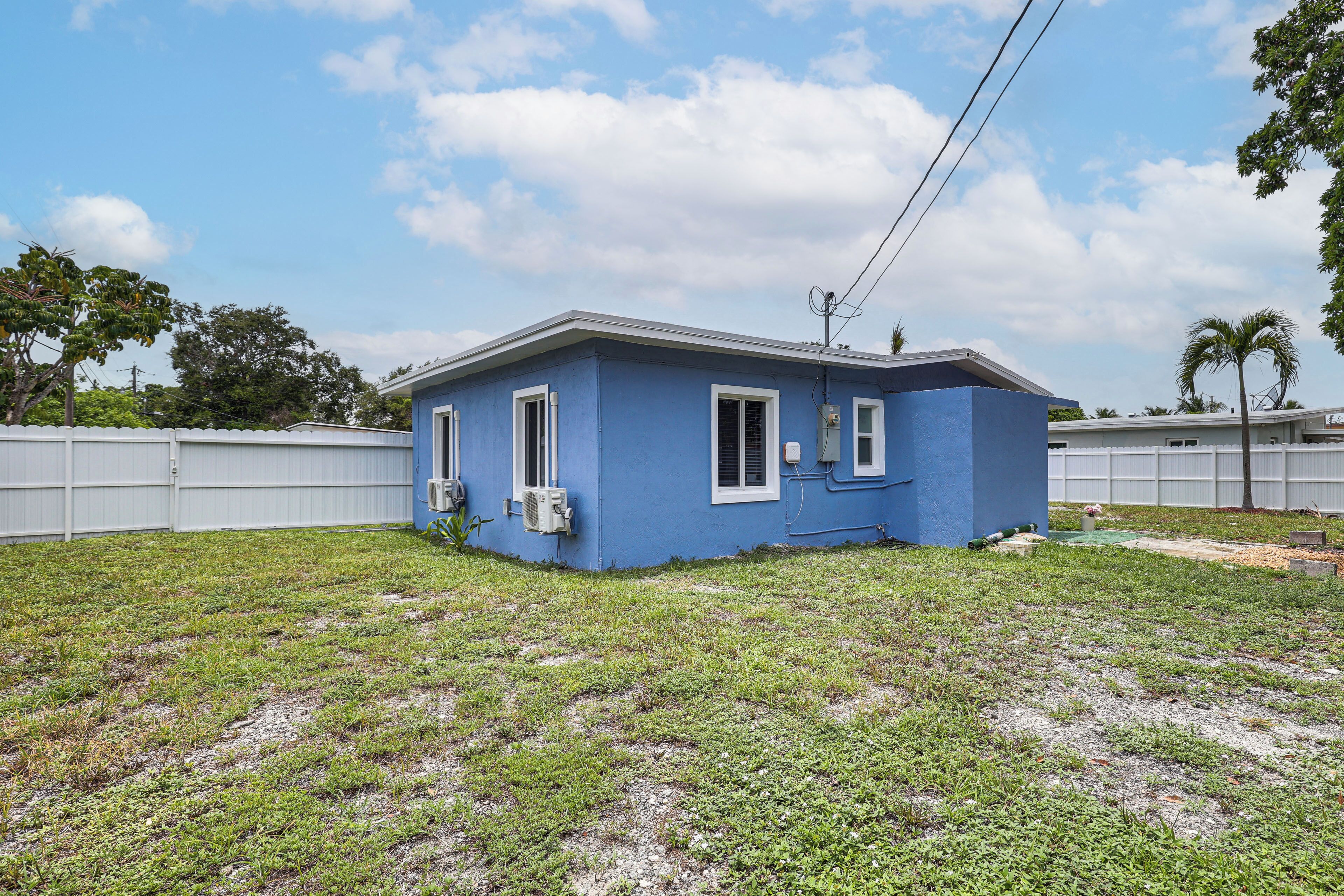 A small blue house with a fenced yard, a single window, and an air conditioning unit.