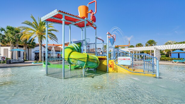 A water park with a green slide, a water jet, and a pool area. - Pool & Lazy River: Windsor House 9 Mi to Disney! (Kissimmee)