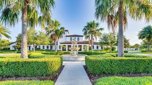 A well-maintained garden with a central fountain, palm trees, and a pathway leading to a building with a tiled roof. - Pool & Lazy River: Windsor House 9 Mi to Disney! (Kissimmee)