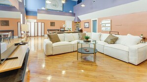 A spacious living area with a sectional sofa, a glass coffee table, and a wooden floor. There is a kitchen area in the background with a refrigerator and a sink. - Downtown Apt: 23 Mi to Hocking Hills State Park (Lancaster)