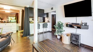 A modern living room with a wooden floor, a black leather sofa, a dining table, a flat-screen TV, a fireplace, and a kitchen area in the background. - Walk to Virginia Lake: Reno Condo w/ Balcony! (Reno)