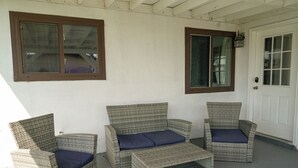 Een veranda met drie rieten stoelen en een kleine tafel, elk voorzien van een blauw kussen.