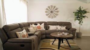 Een moderne woonkamer met een bruine leren modulaire bank, een ronde salontafel en een decoratief wandobject.