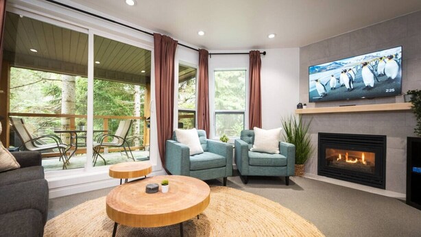 Un salon moderne doté d’une cheminée, de sièges confortables, d’un téléviseur et de grandes fenêtres offrant une vue sur l’extérieur.