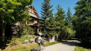 Un cycliste circule sur une piste aménagée, le long d’un bâtiment dont la façade est en bois et qui possède un mur en pierre.