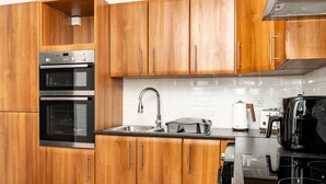 A modern kitchen with wooden cabinets, stainless steel appliances, and a black countertop. - Hilltown by Central Serviced Apartments (Dundee)