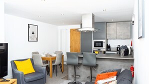 Uma sala de estar moderna com um sofá cinza, uma mesa de jantar de madeira e uma cozinha com armários cinza e micro-ondas.