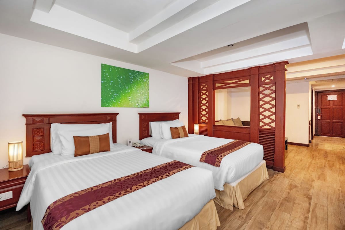 A hotel room with two beds, a green wall art, a wooden partition, and a wooden floor.