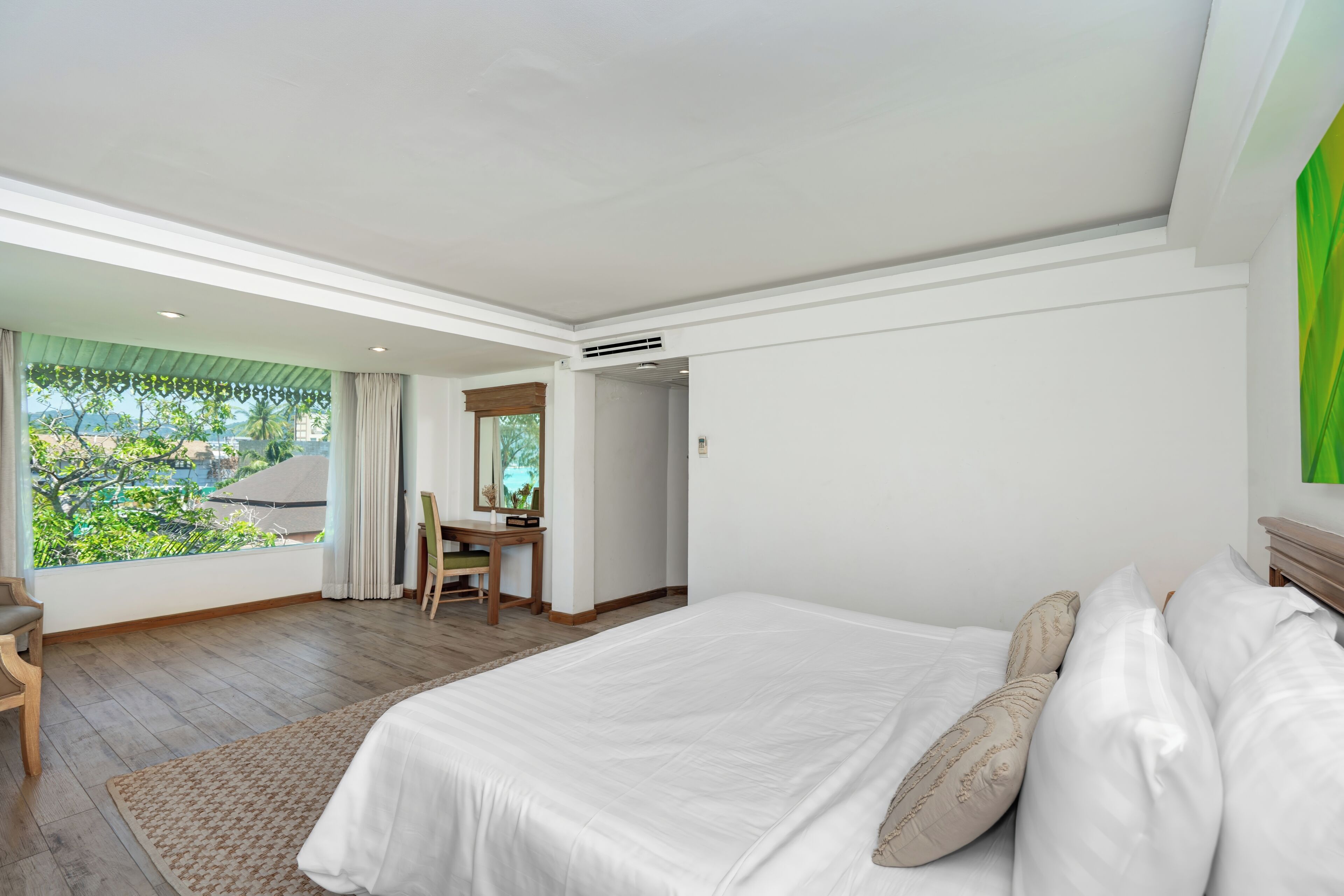A bedroom with a large bed, a desk, and a view of greenery outside.