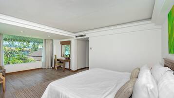 A bedroom with a large bed, a desk, and a view of greenery outside.