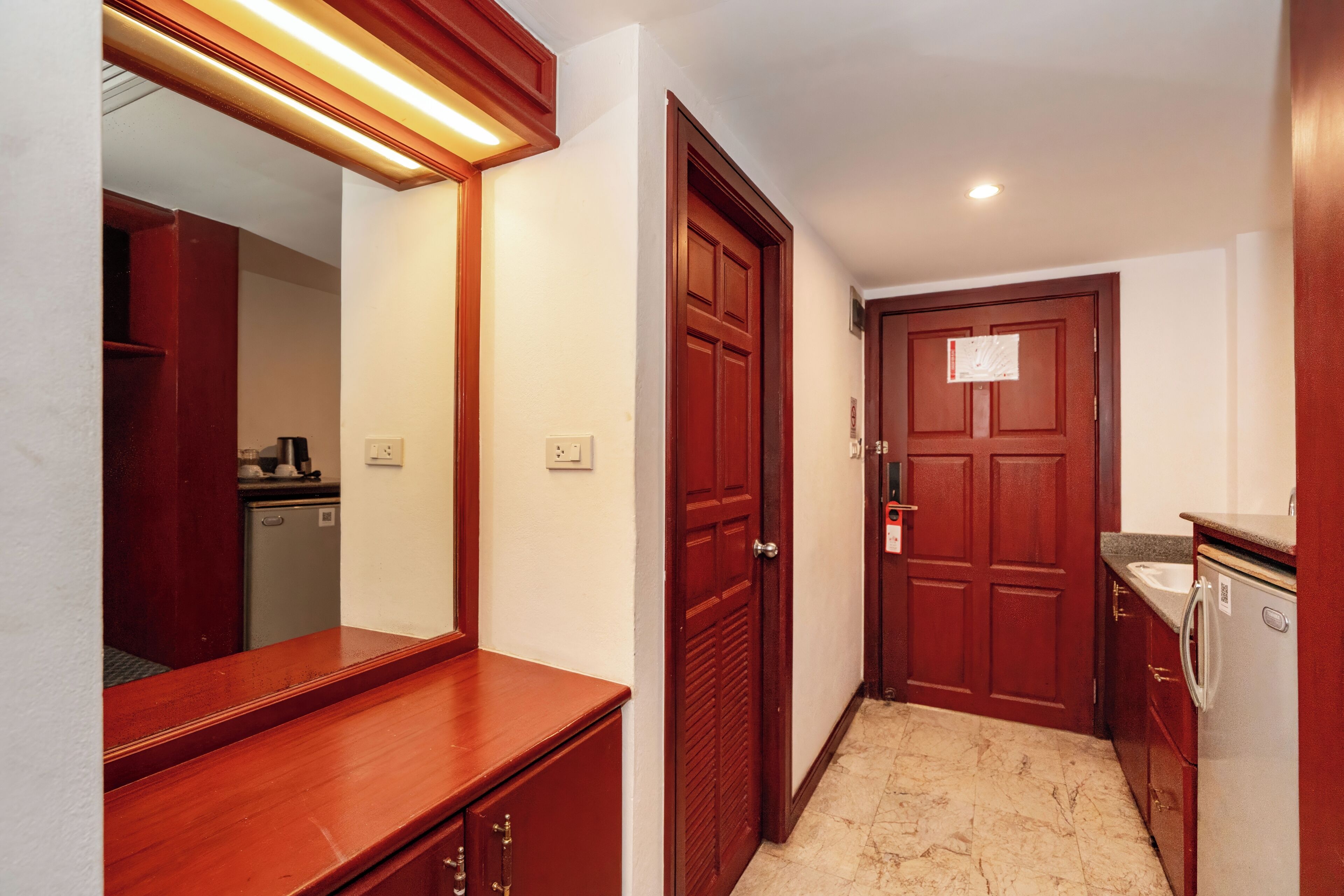 A hallway with a wooden counter, a mirror, a door, and a refrigerator.