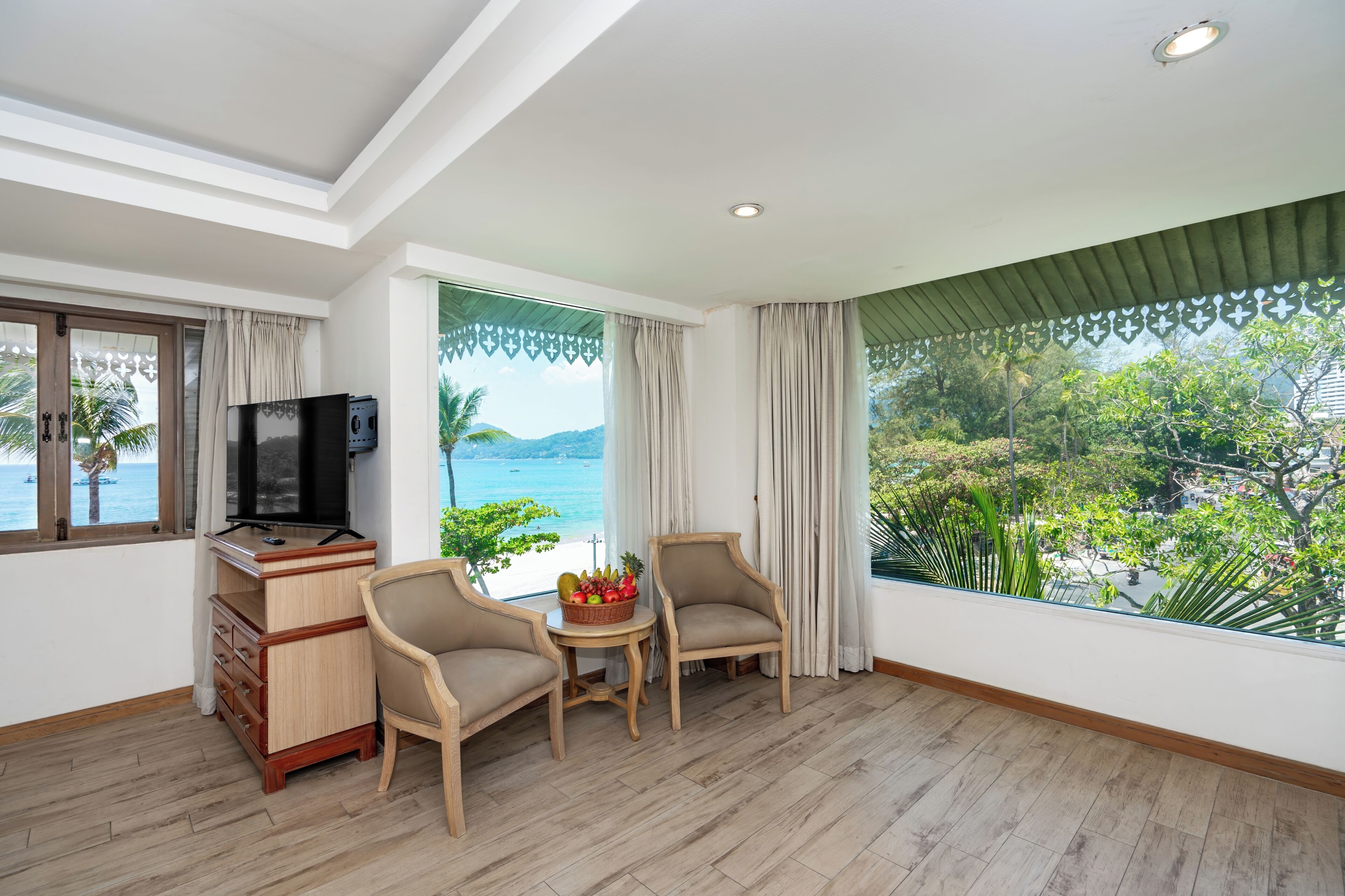 Habitación con televisión, muebles de madera, una mesita con fruta y vista al mar.