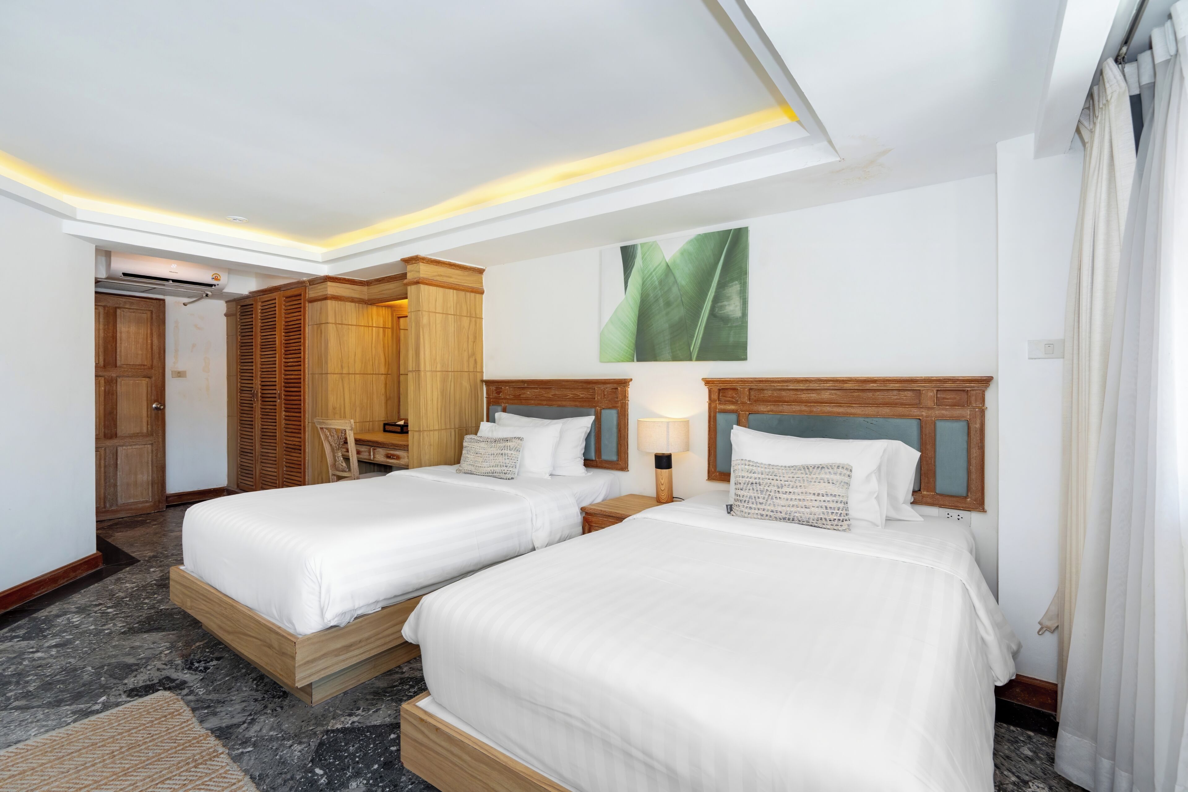 Habitación de hotel con dos camas, un armario de madera, un espejo, aire acondicionado de pared y una lámpara en el techo.