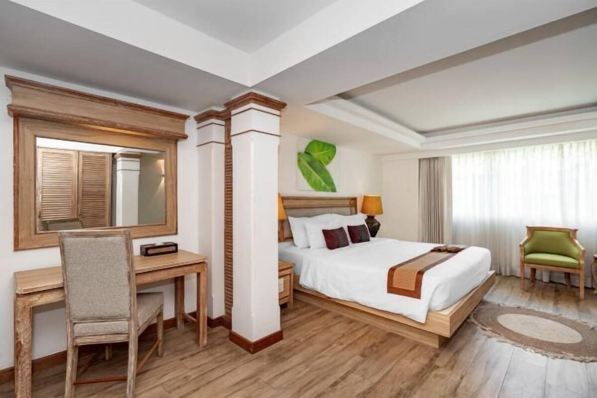 Habitación de hotel con cama, escritorio, silla y un espejo grande.