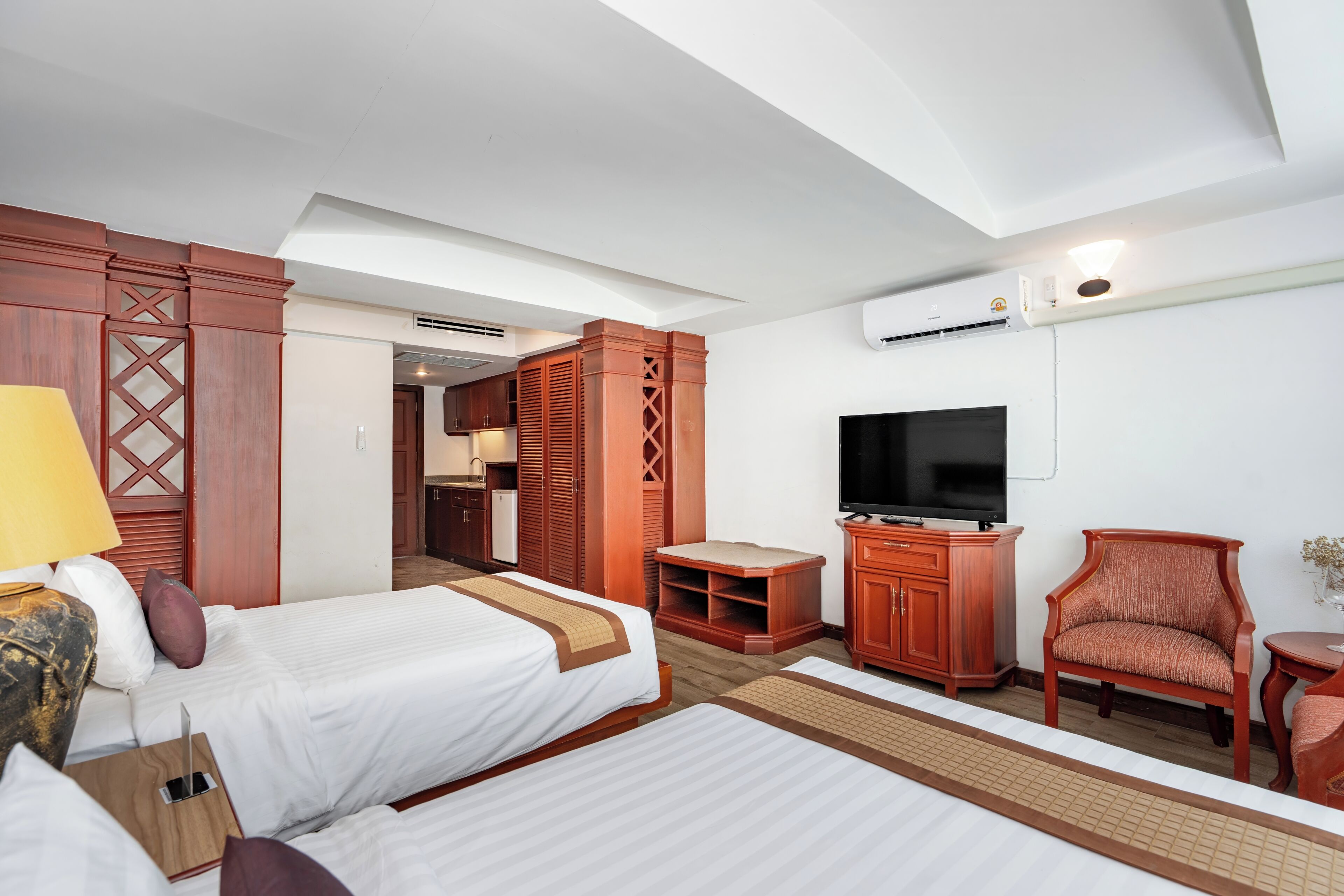 Ein Hotelzimmer mit zwei Betten, einem Fernseher, Holzmöbeln und einer Klimaanlage.