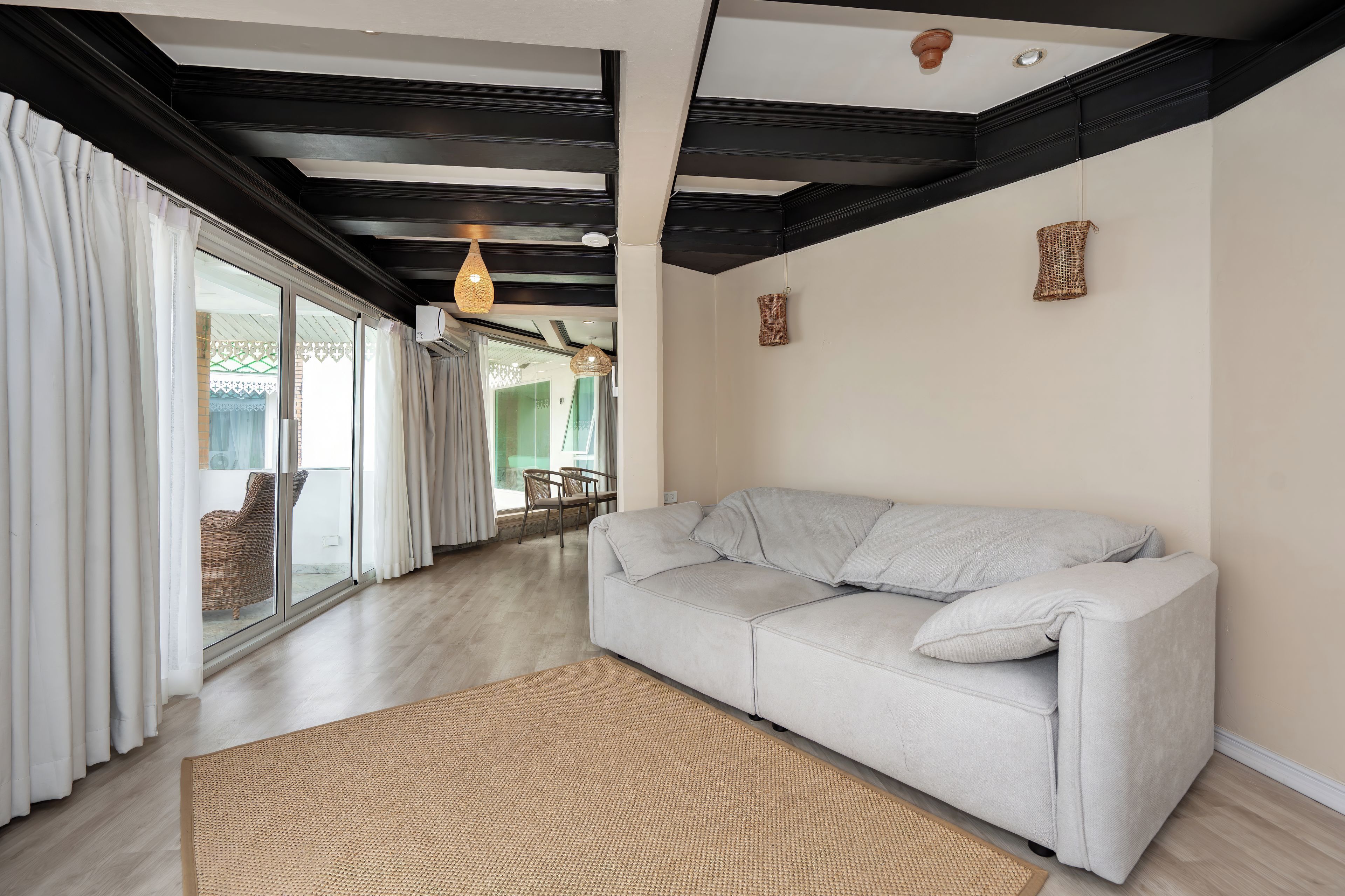 A modern living room with a sofa, a woven rug, and a ceiling with exposed beams.