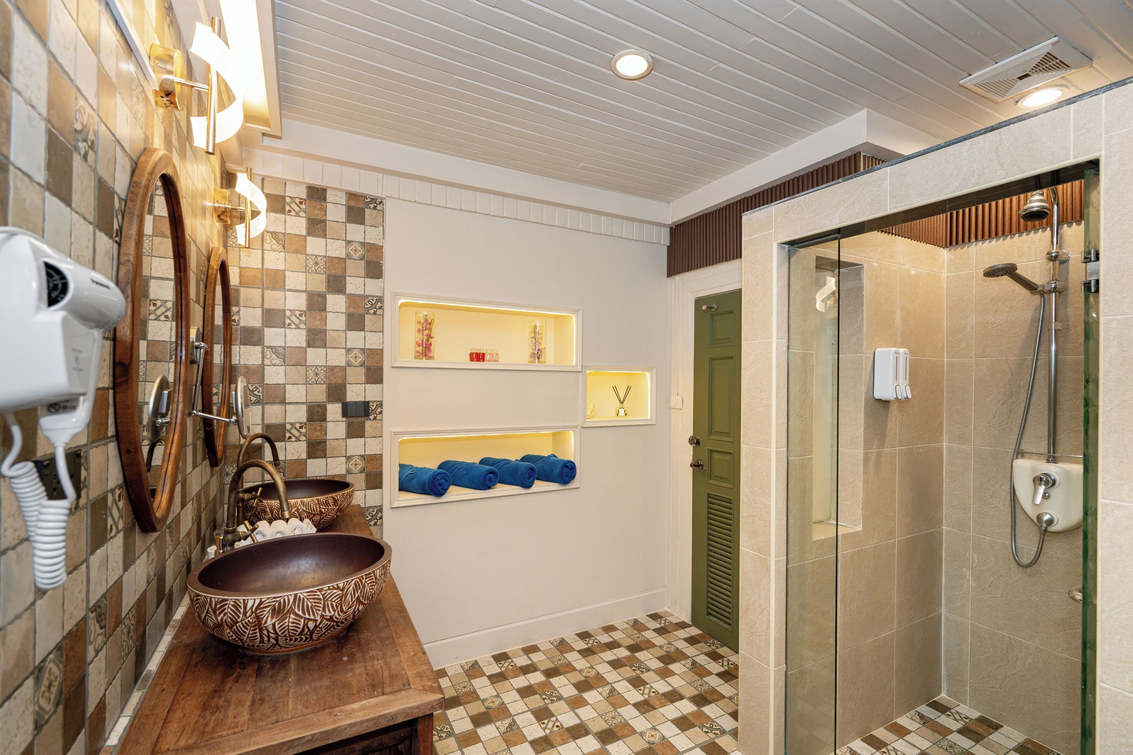 A bathroom with a wooden vanity, a large bowl sink, a hairdryer, and a glass-enclosed shower.