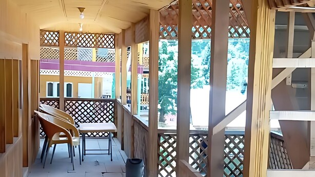 A covered wooden deck with chairs and tables, wooden railings, and a view of the outside. - Green Land Guest House (Taobat)