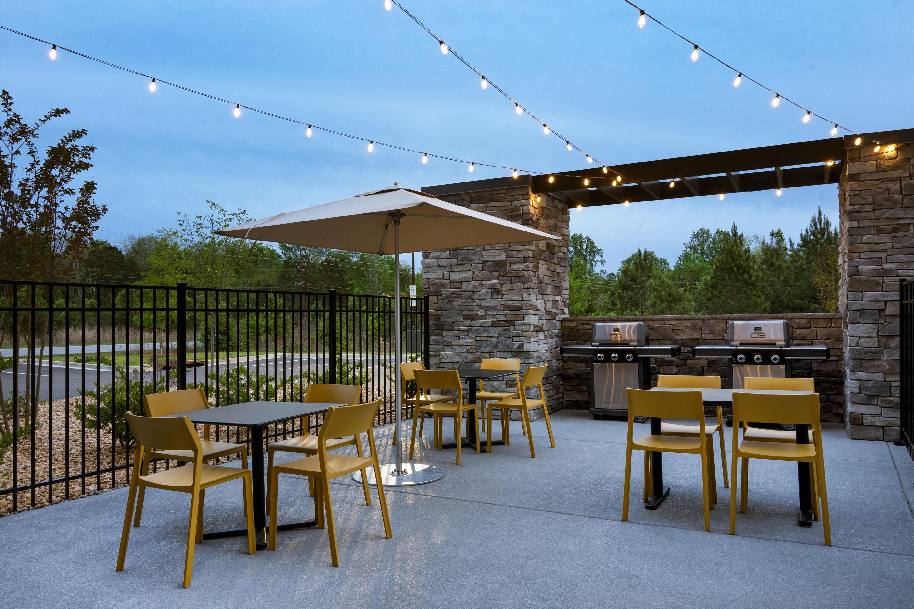 An outdoor patio with tables and chairs, string lights, a stone wall, and a grill.