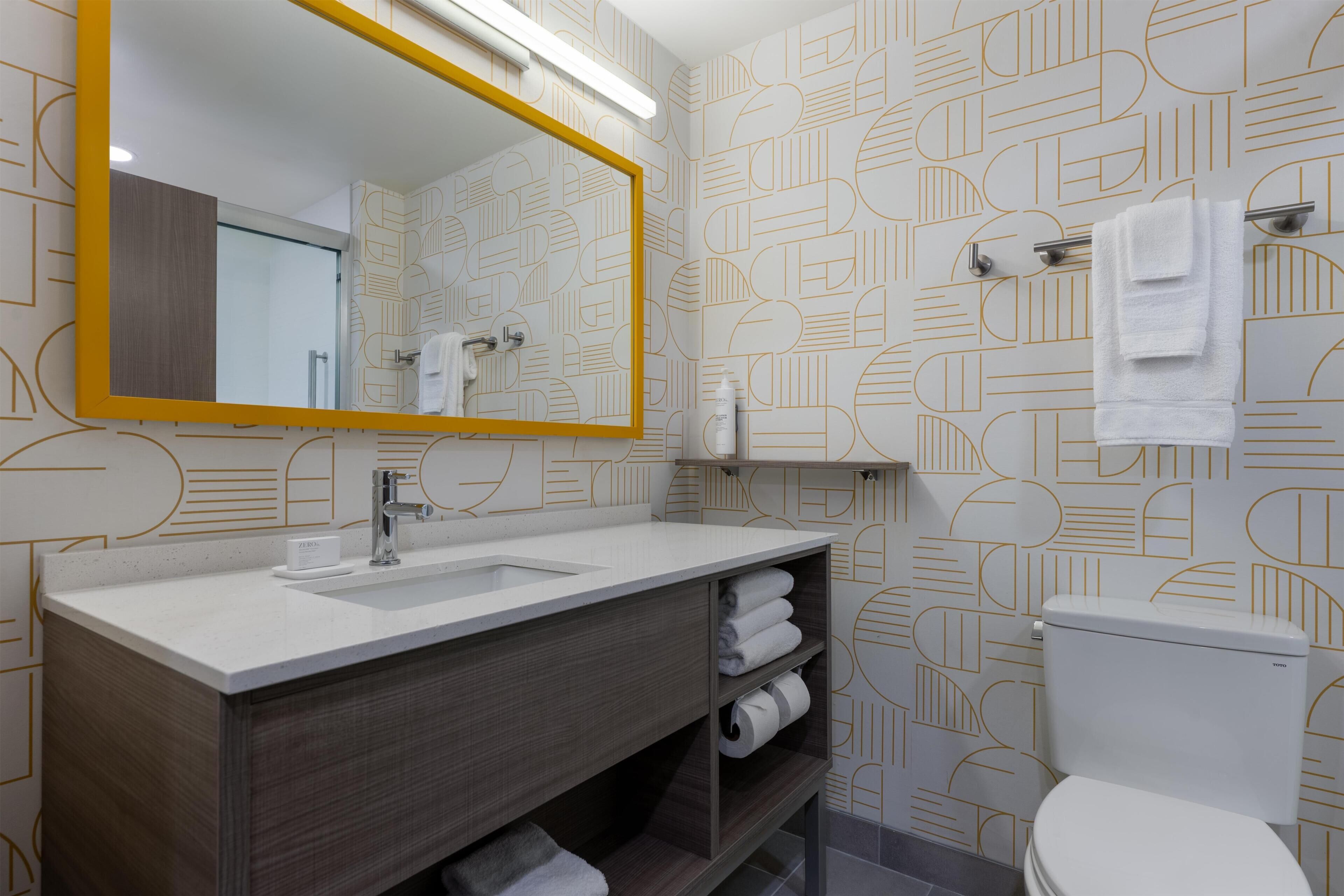 Une salle de bain moderne avec un grand miroir, un lavabo, des toilettes et un porte-serviettes.