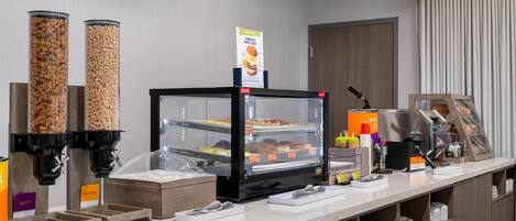 A buffet area with a self-serve station, a display case with pastries, and a sign indicating a sweet treat.