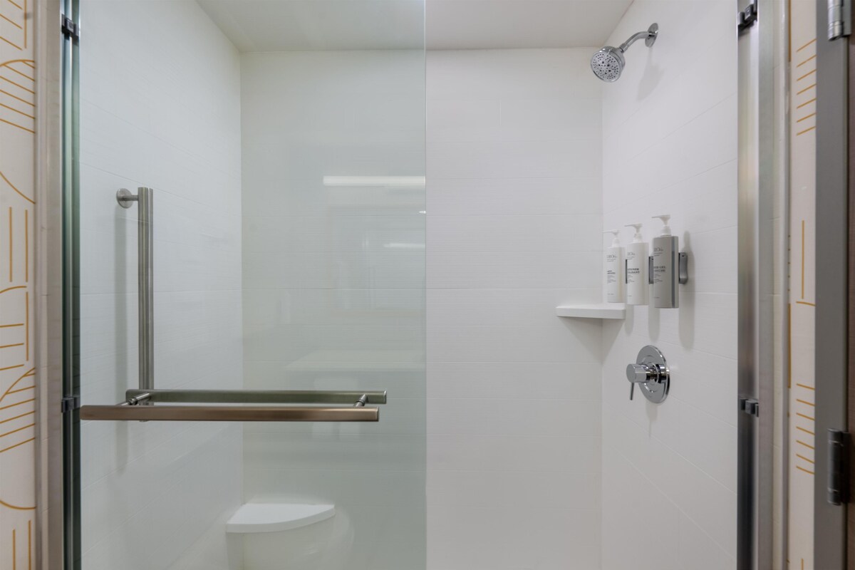 A modern bathroom with a glass shower enclosure, a toilet, and a shelf with toiletries.