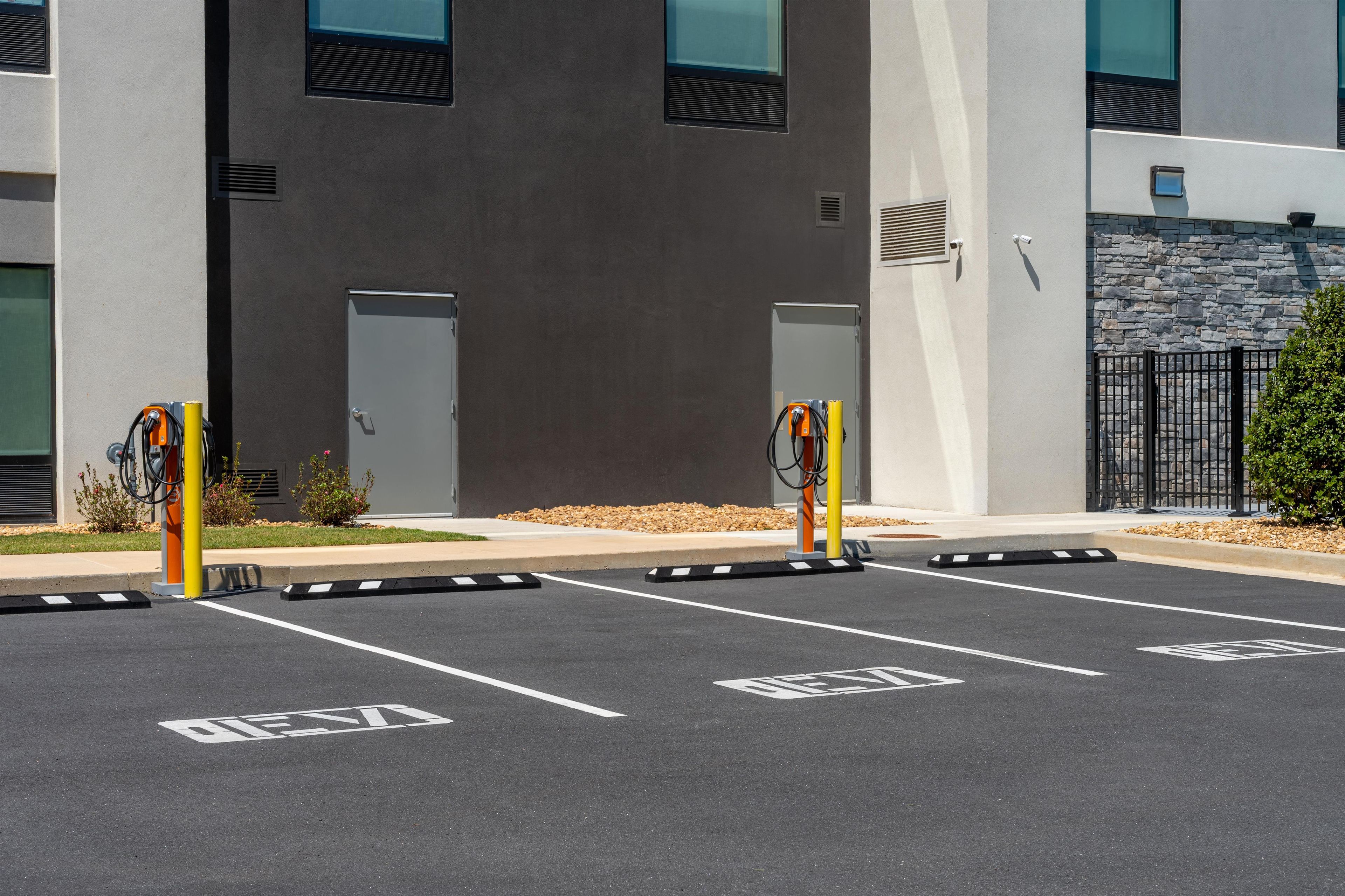 A parking area with electric vehicle charging stations, marked parking spaces, and a building with a stone facade.