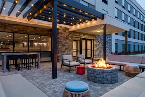 Un patio al aire libre con un brasero, asientos y una zona cubierta con luces colgantes.