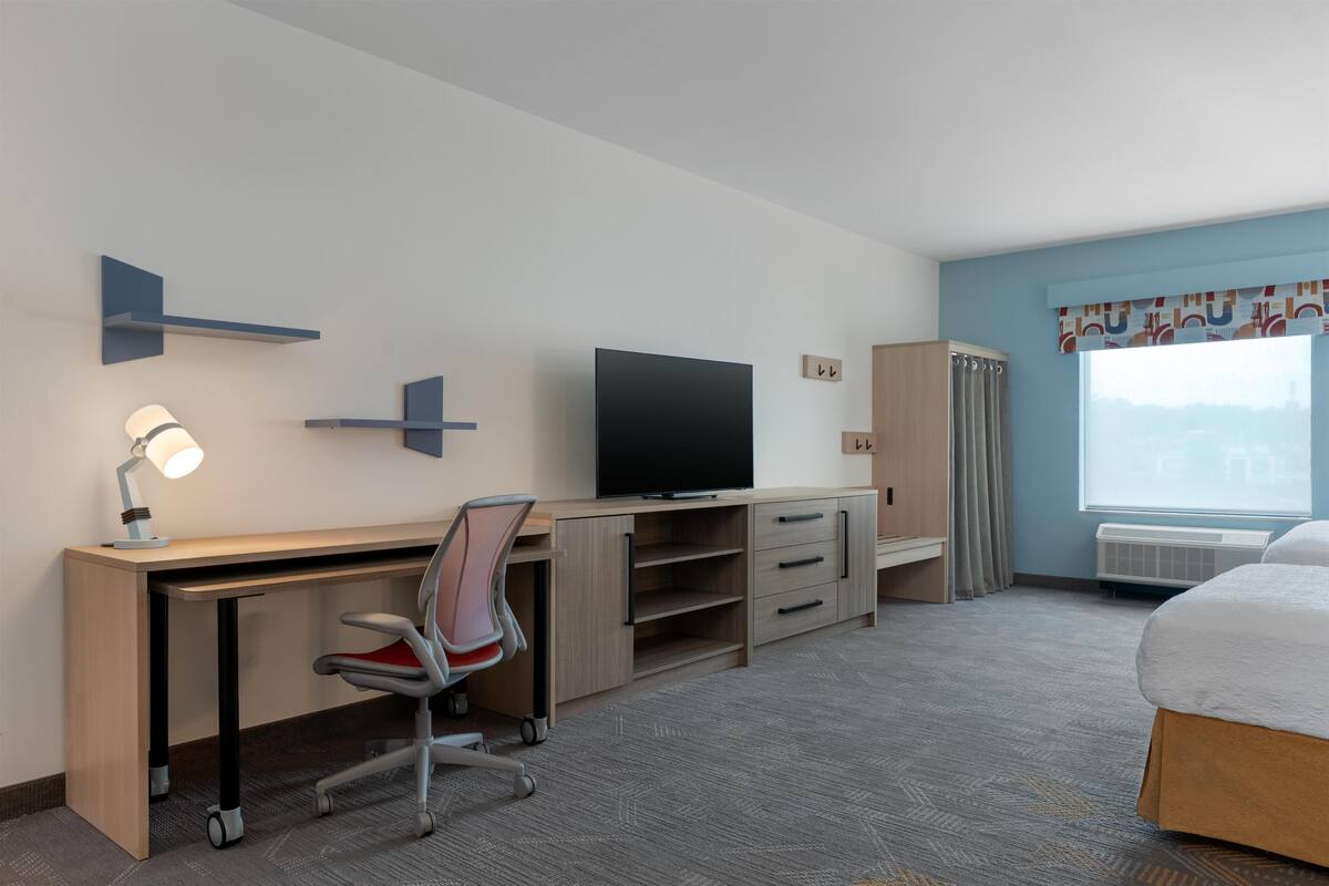 Une chambre d’hôtel équipée d’un bureau, d’une chaise, d’une télévision, d’une armoire et d’un lit.