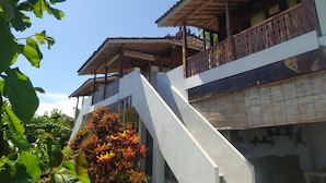 A multi-story building with a balcony, a staircase, and a garden area with flowering plants. - Villa Joglo Paris Yogyakarta (Parangtritis)