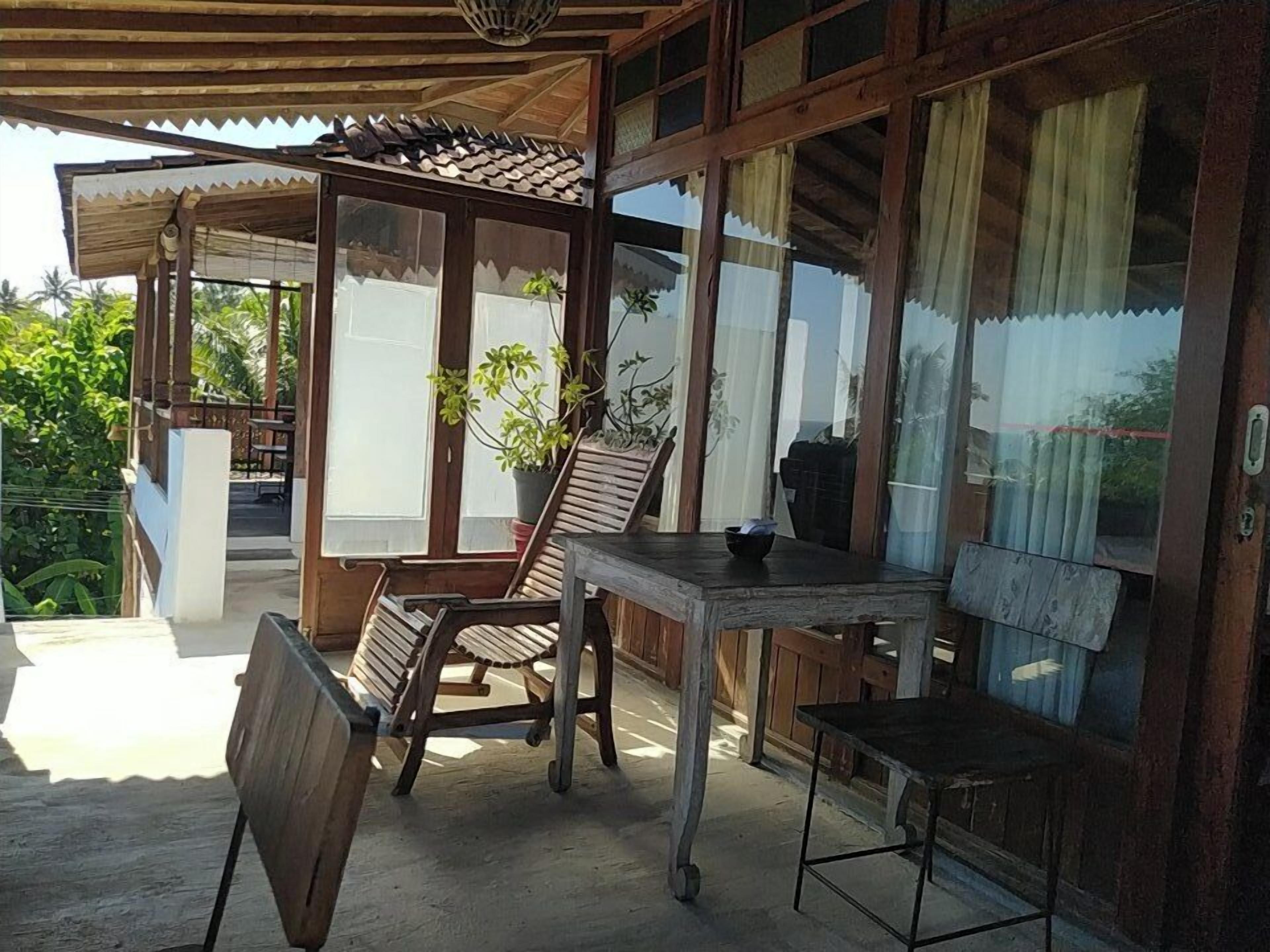 A wooden outdoor seating area with a table and chairs, a potted plant, and a view of greenery.