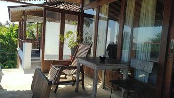 A wooden outdoor seating area with a table and chairs, a potted plant, and a view of greenery.