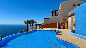 A pool area with a view of the sea, a building with balconies, and a tiled wall.