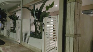 Una entrada con portón, un cartel azul indicando dirección, un coche estacionado y una planta en maceta.