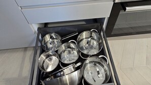 Una cocina con estufa a gas, encimera blanca y un cajón con utensilios de cocina de acero inoxidable.